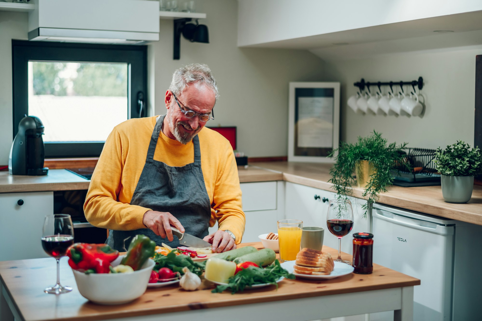 Senior man in apron preparing food at the kitchen counter and cooking a meal