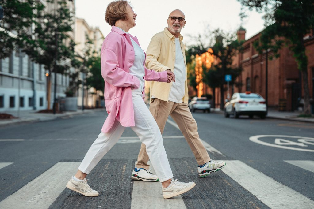 Happy senior couple holding hands and walking across a pedestrian crossing in an urban street.